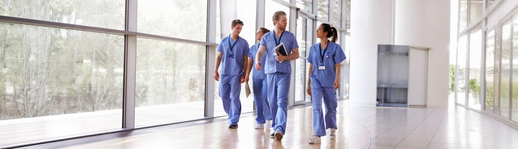 Four healthcare workers in scrubs walking in corridor